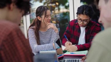 Kütüphanede iki üniversite öğrencisi kameraya bakıp gülümsüyor ve kampüste ders çalışıyor. Asyalı ve İspanyol sınıf arkadaşları.