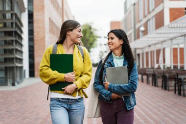 Dersten sonra kampüste yürüyüp konuşan neşeli, çok kültürlü öğrenci kızlar. 