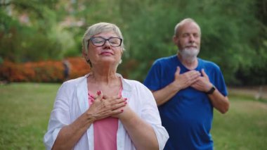 Sağlıklı yaşlı çift göğüs kafesinde el ele tutuşuyor, temiz hava soluyor, yoga esnemesinden sonra dinleniyor, farkındalık ve meditasyon uyguluyor.