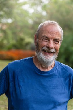 Portrait of happy senior man in park wearing blue t-shirt, smiling after doing some healthy active sport