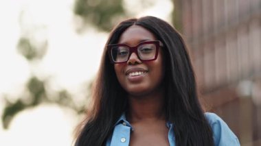 Afro-Amerikan üniversite kız öğrencisinin portresi üniversitenin dışındaki kameraya bakıyor.