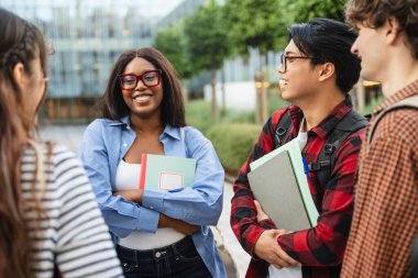 Afrika kökenli Amerikalı kız öğrenci ve grup arkadaşları üniversite binasının önünde toplanıp okul projesi hakkında konuşuyorlar. 