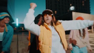 Trendy woman with group of friends performing urban breakdance music having fun at night in the city