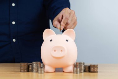 Man hand inserting coin inside of piggy bank with coin stack. Concept for invest and saving success in the future goal