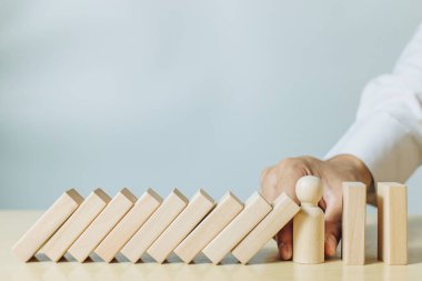 Tahta insan modelini elinde tutan bir adam domino taşlarını durduruyor. Risk yönetimi, risk koruması, kriz ve yatırım koruması kavramı