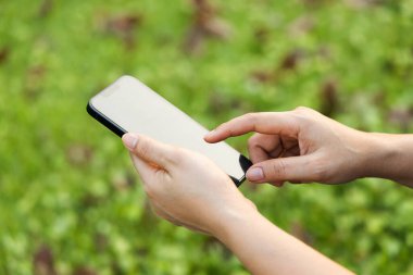 Yakın plan el ele tutuşmalar, arka planda akıllı telefonlar. Şehir parkında cep telefonu kullanan kadın.