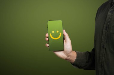 Hizmet derecesi, memnuniyet ve geri bildirim konsepti. Servis deneyimi için gülümseyen yüz ifadeleri gösteren cep telefonu tutan bir adam