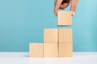 İş büyümesi ya da başarı süreci kavramı. Merdivenler gibi dizilmiş tahta küpün son parçasını da elle yerleştirdim.