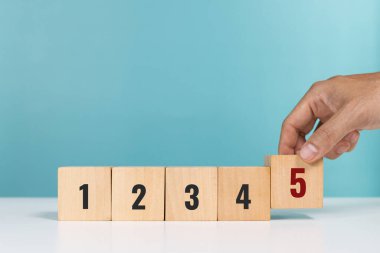 Faaliyetlerin önceliği. Görev önceliği ve yönetim kavramı. Beş numaralı tahta küpleri yerleştiren bir adam öncelik olarak aktiviteleri veya olumlu geri bildirimleri gösterir