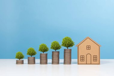 Para tasarrufu, gayrimenkul yatırımı ve ev için yatırım. Bozuk paralar ve büyüyen ağaçlarla dolu küçük bir model ev. Para, emlak yatırımlarının büyüdüğünü gösteriyor.