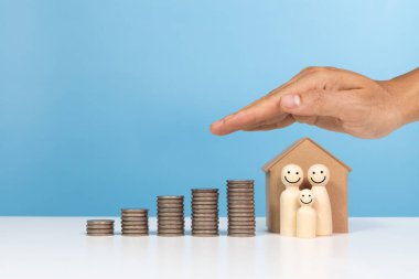 Mülkü, aileyi, ev yatırımını ve mali tasarruf kavramını koru. Minyatür bir evin çatısını koruyan el ve aile mutlu yüzler artan madeni para yığınları