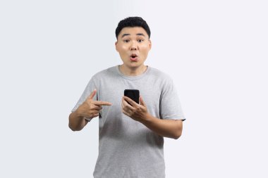 Gülümseme portresi mutlu adam beyaz arka planda duran akıllı telefonu işaret ediyor. Kameraya bakan bir adam inanılmaz bir ifade sergiliyor.