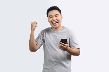 Heyecanlı adam portresi kamera ve eli bir yumruğa yapışmış ve diğer el beyaz arka planda izole akıllı telefonu tutuyor.