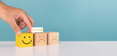 Memnuniyet, hizmet derecesi ve olumlu geri bildirim kavramı. Bir erkek mükemmel bir değerlendirme için gülen surat ifadeli tahta bloğu seçer. Servise beş yıldızlı bir not ver.