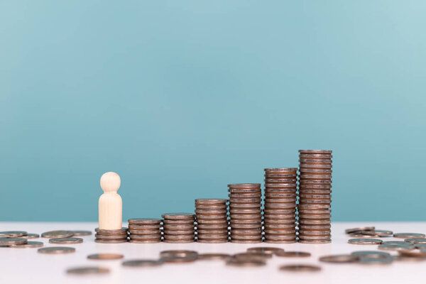 A wooden human figure stands next to a series of ascending stacks of coins, symbolizing personal financial growth, investment journey, and economic development over time