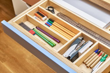 Table for children with multi-colored facades of roll-out drawers for stationery. Sawhorse desk made of plywood and solid oak close view clipart