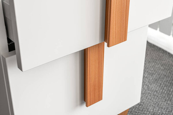 Stylish white office commode with wooden handles and legs with open empty drawers closeup view. Comfortable furniture for home and office furnishing