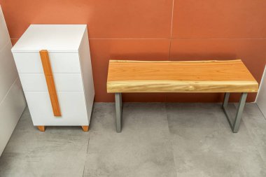 Live edge wooden bench with gray metal legs and white chest of drawers with wooden handles and legs in bathroom clipart