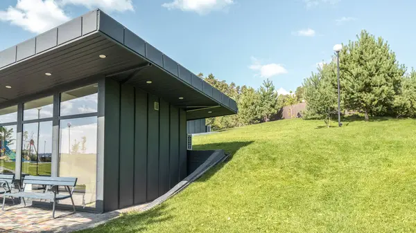 stock image Modern guest house with standing seam facade panoramic glazing and large flat roof overhang in park. Minimalist architectural style of public building