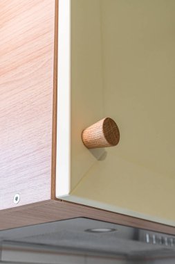 Wooden handle attached to yellow sleek kitchen cabinet with a simple design. Solid oak cabinet knob close up view clipart