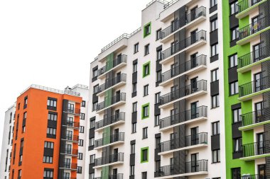 Turuncu, yeşil ve beyaz cepheli modern apartmanlar, büyük pencereler, metal parmaklıklı balkonlar, bulutlu bir gökyüzüne karşı, kentsel yaşam