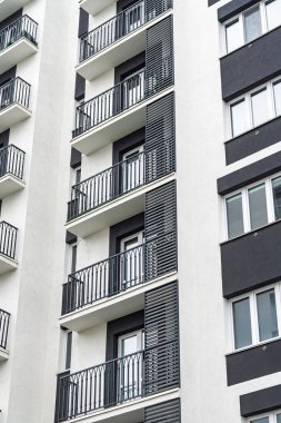 Siyah korkuluklu, beyaz ve gri tonlu, kentsel konut mimarisi tasarımı sergilenen modern bir apartman cephesi.