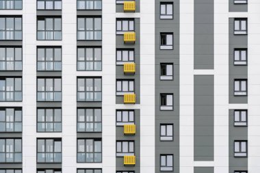 Sarı ve gri aksanlı çağdaş bina cephesi, minimalist tasarım, pencereler ve balkonlar, bulutlu bir gökyüzüne karşı, ön yakın görüş