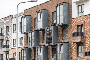 Çağdaş apartman cephesi, renkli tuğla duvarlar, pencereler ve çıkıntılı gri balkonlar. Kentsel konut kavramı