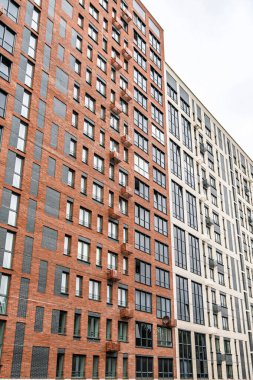 Bej, kırmızı tuğla ve cam cepheli modern çok katlı binalar, balkon ve pencereler sergileniyor. Kentsel mimari konsepti, düşük açı görünümü