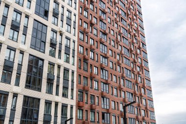 Bej, kırmızı tuğla ve cam cepheli modern çok katlı binalar, balkon ve pencereler sergileniyor. Kentsel mimari konsepti, düşük açı görünümü