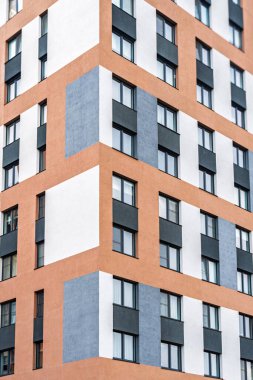 Modern apartman cephesi, turuncu, beyaz ve gri tonlu, koyu çerçeveli camlı ve renkli aksanlı. Kentsel konut kavramı