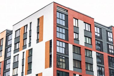 Modern apartman cephesi, beyaz, turuncu ve kırmızı tonlu, koyu çerçeveli pencereli, düşük açılı manzaralı. Kentsel konut kavramı
