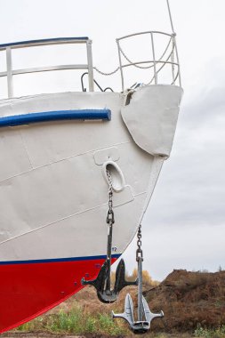 Geminin pruvası, kırmızı ve beyaz bir gövde, iki büyük çapa tarafından çevrelenmiş, yakın planda. Gemi bakım için karaya yanaştı.
