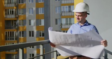 Yetişkin mimar tasarımcı balkonda duran konut kompleksinin çizimlerine bakıyor. Mühendis apartman bloğu projesinde çalışmaktan hoşlanıyor