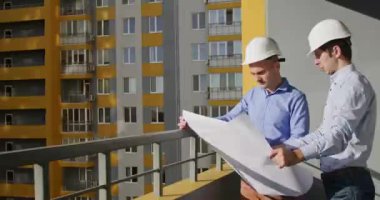Erkek mimar, konut kompleksi inşası hakkında mühendis meslektaşını dinler. Becerikli inşaatçı, tasarım dairelerine bitmiş çizimleri bloklamasını açıklıyor