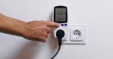 Adam wattmetreyi açıyor ve elektrikli aletin güç tüketimini kontrol ediyor ve akıllı telefona bakarak işlevini yerine getiriyor. Sorunu düzeltmeye çalışan kişi