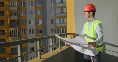 Mimar parlak güneş ışığında konut kompleksini inceler. Kırmızı şapka takan erkek müteahhit, çizimlerdeki ve gerçek binalardaki ölçümleri karşılaştırıyor