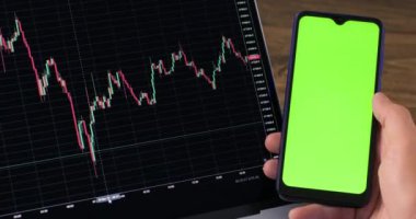 Freelancer dizüstü bilgisayarda grafiği inceler ve sonuçları karşılaştırır. İşadamı yeşil renkli ekranlı akıllı telefon aracılığıyla şifreleme para birimini başarılı bir şekilde satın aldı