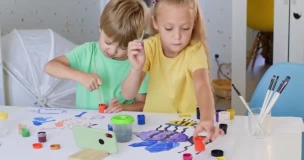 蹒跚学步的男孩 学龄前儿童和女孩准备在家里一起粉刷画图 姐姐跟哥哥讲用画笔画画的事 — 图库视频影像