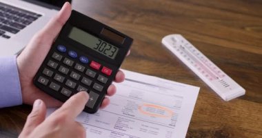 İşadamı, elektrik faturaları ve sabit sıcaklık kontrolünden elde edilen bilgileri karşılaştırıyor. Daire sahibi hesap makinesinde matematik denklemlerini sayar