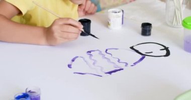 Preschooler girl paints picture with black and blue colours on large paper sheet. Child enjoys painting pictures and spending weekend art home