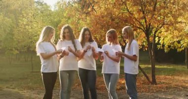 Teenage girls with excited and amused expression launch paper airplanes in city park illuminated by sunset. Teenagers show nice friendship