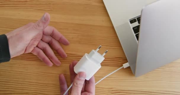 人在木制桌子上显示出连接笔记本电脑插头的绳索 移动设备收费的配件 电气技术 — 图库视频影像