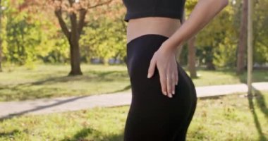 Şehir parkında güneş ışığıyla aydınlatılmış enerji dolu siyah spor elbise giyen genç bir kadın. Kısa saçlı sporcu kadın sağlığıyla ilgilenmekten hoşlanıyor.