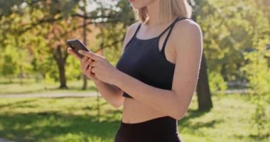 Genç bir kadın telefon uygulamasında ilerleme kaydediyor. Gülümseyen sporcu kadın, sonbahar parkında koşmanın mükemmel sonuçlarını göreceği için heyecanlı.