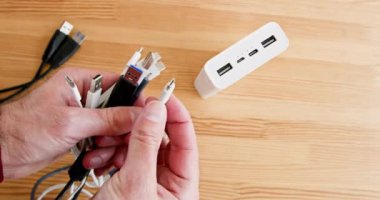 Adam elektrik direği için doğru kabloyu ahşap masanın üzerinden seçiyor. USB, şarj olan aygıtlar için kablolar üzerindeki türleri ekler. Elektrik ekipmanları