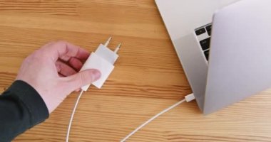 Erkek el, kabloyu dizüstü bilgisayara bağlı olarak ahşap masa üst görüşüne yerleştirir. Dijital aygıtlar için elektrik aksesuarları