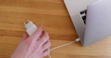 Adam adaptörü çıkarır ve taşınabilir bataryayı masa kapatma ekranındaki laptopa takar. Ofiste Power Bank kullanılıyor. Elektrik malzemeleri.
