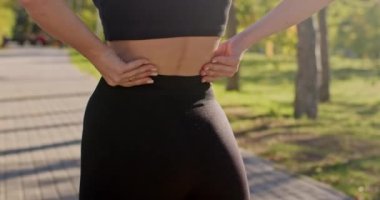 Genç sporcunun güneş ışığıyla aydınlatılan uzun koşudan dolayı sırt ağrısı var. Siyah spor kıyafeti giyen bir kadın.