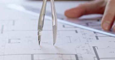 Mühendis elleri inşaat planındaki bölmeleri kullanarak daire çiziyor. İşçi masa üzerinde yatarken çember çapını ölçmek için cetvel kullanır